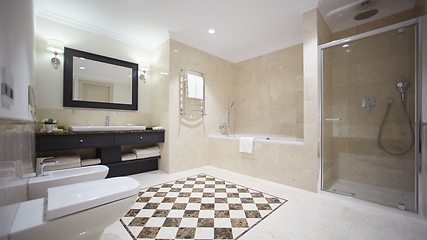 Image showing Nice bathroom in a modern style with gray tiled walls. There is a white bath with a glass partition, shower, mirrors, light sink, toilet and a bidet, luminous lamps