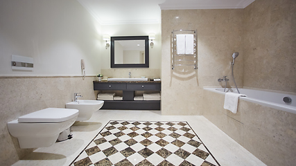 Image showing Nice bathroom in a modern style with gray tiled walls. There is a white bath with a glass partition, shower, mirrors, light sink, toilet and a bidet, luminous lamps