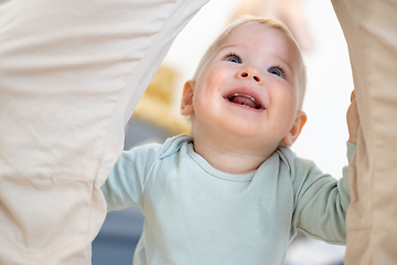 Image showing Portrait of adorable cheerful infant baby boy child taking first steps holding to father's pants at home. Cute baby boy learning to walk.