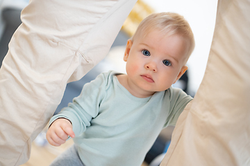 Image showing Portrait of adorable curious infant baby boy child taking first steps holding to father's pants at home. Cute baby boy learning to walk.