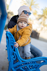 Image showing Young mother with her cute infant baby boy child on bench in city park.