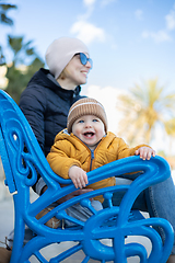 Image showing Young mother with her cute infant baby boy child on bench in city park.