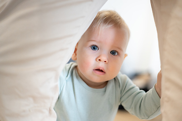 Image showing Portrait of adorable curious infant baby boy child taking first steps holding to father's pants at home. Cute baby boy learning to walk.