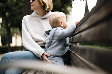 Image showing Young mother with her cute infant baby boy child sitting on bench in city park.