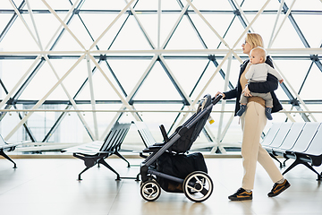 Image showing Mother carying his infant baby boy child, pushing stroller at airport departure terminal moving to boarding gates to board an airplane. Family travel with baby concept.