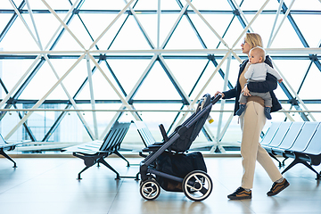 Image showing Mother carying his infant baby boy child, pushing stroller at airport departure terminal moving to boarding gates to board an airplane. Family travel with baby concept.