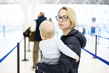 Image showing Mother carying his infant baby boy child queuing at airport terminal in passport control line at immigrations departure before moving to boarding gates to board an airplane. Travel with baby concept.