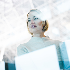 Image showing Portrait of strong, determined, successful young woman looking trough window while waiting to board an airplane at airport terminal departure gates.