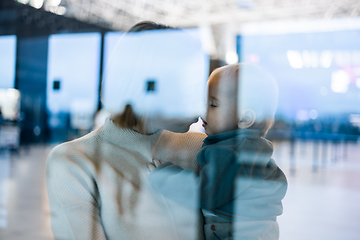 Image showing Thoughtful young mother kissing and caressing his infant baby boy child while waiting by the window at airport terminal departure gates. Travel with baby concept.