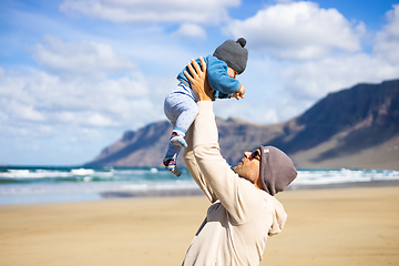 Image showing Father enjoying pure nature holding and playing with his infant baby boy son in on windy sandy beach of Famara, Lanzarote island, Spain. Family travel and parenting concept.