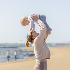 Image showing Mother enjoying summer vacations holding, playing and lifting his infant baby boy son high in the air on sandy beach on Lanzarote island, Spain. Family travel and vacations concept.