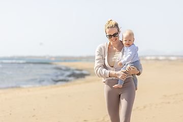 Image showing Mother holding and carrying his infant baby boy son on sandy beach enjoying summer vacationson on Lanzarote island, Spain. Family travel and vacations concept.