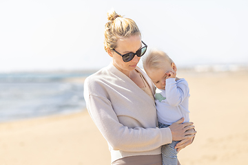 Image showing Mother holding and carrying his infant baby boy son on sandy beach enjoying summer vacationson on Lanzarote island, Spain. Family travel and vacations concept.