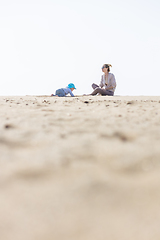 Image showing Mother playing his infant baby boy son on sandy beach enjoying summer vacationson on Lanzarote island, Spain. Family travel and vacations concept.