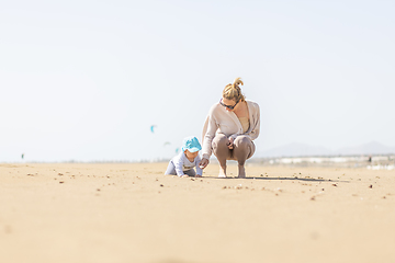 Image showing Mother playing his infant baby boy son on sandy beach enjoying summer vacationson on Lanzarote island, Spain. Family travel and vacations concept.