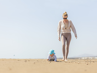 Image showing Mother playing his infant baby boy son on sandy beach enjoying summer vacationson on Lanzarote island, Spain. Family travel and vacations concept.