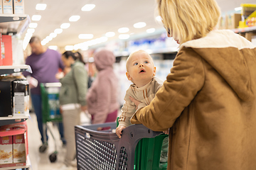 Image showing Casualy dressed mother choosing products in department of supermarket grocery store with her infant baby boy child in shopping cart.