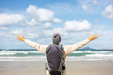 Image showing Young father rising hands to the sky while enjoying pure nature carrying his infant baby boy son in backpack on windy sandy beach of Famara, Lanzarote island, Spain. Family travel concept.