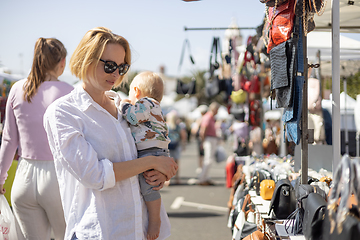 Image showing Mother hoding his infant baby boy child whilechecing items at sunday flea market.