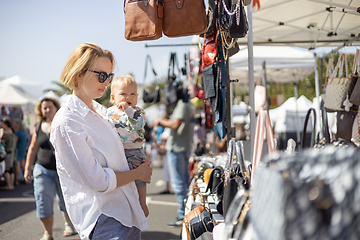 Image showing Mother hoding his infant baby boy child whilechecing items at sunday flea market.