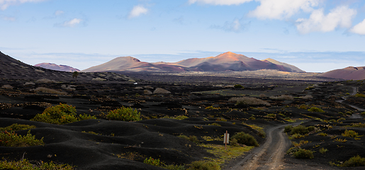 Image showing Black volcanic landscape of La Geria wine growing region with view of Timanfaya National Park in Lanzarote. Popular touristic attraction in Lanzarote island, Canary Islands, Spain.