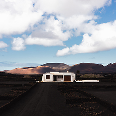 Image showing Traditional white house in black volcanic landscape of La Geria wine growing region with view of Timanfaya National Park in Lanzarote. Touristic attraction in Lanzarote island, Canary Islands, Spain.