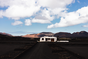 Image showing Traditional white house in black volcanic landscape of La Geria wine growing region with view of Timanfaya National Park in Lanzarote. Touristic attraction in Lanzarote island, Canary Islands, Spain.