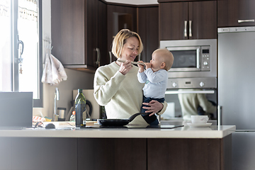 Image showing Happy mother and little infant baby boy cooking and tasting healthy dinner in domestic kitchen. Family, lifestyle, domestic life, food, healthy eating and people concept.