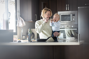 Image showing Happy mother and little infant baby boy cooking and tasting healthy dinner in domestic kitchen. Family, lifestyle, domestic life, food, healthy eating and people concept.