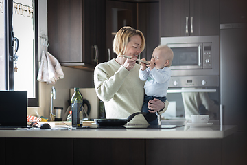 Image showing Happy mother and little infant baby boy cooking and tasting healthy dinner in domestic kitchen. Family, lifestyle, domestic life, food, healthy eating and people concept.