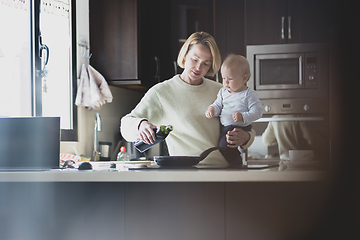 Image showing Happy mother and little infant baby boy together making pancakes for breakfast in domestic kitchen. Family, lifestyle, domestic life, food, healthy eating and people concept.