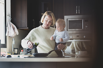 Image showing Happy mother and little infant baby boy together making pancakes for breakfast in domestic kitchen. Family, lifestyle, domestic life, food, healthy eating and people concept.