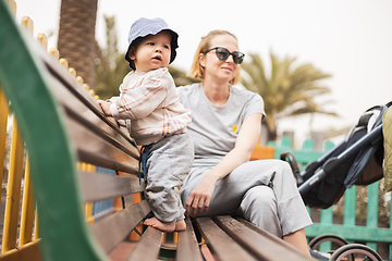 Image showing Young mother with her cute infant baby boy child on bench on urban children's playground on warm summer day.