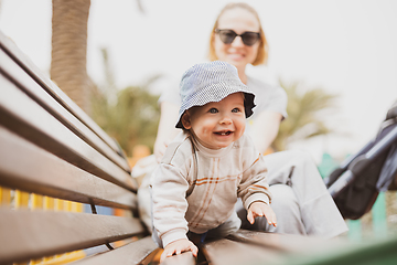 Image showing Young mother with her cute infant baby boy child on bench on urban children's playground on warm summer day.