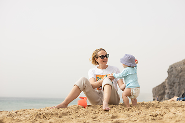 Image showing Mother playing his infant baby boy son on sandy beach enjoying summer vacationson on Lanzarote island, Spain. Family travel and vacations concept.