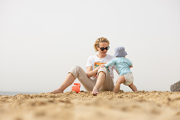 Image showing Mother playing his infant baby boy son on sandy beach enjoying summer vacationson on Lanzarote island, Spain. Family travel and vacations concept.