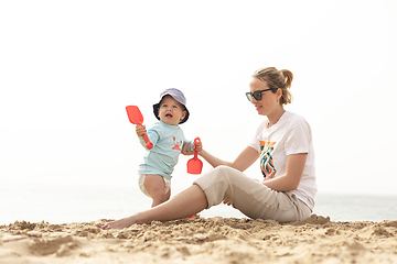 Image showing Mother playing his infant baby boy son on sandy beach enjoying summer vacationson on Lanzarote island, Spain. Family travel and vacations concept.