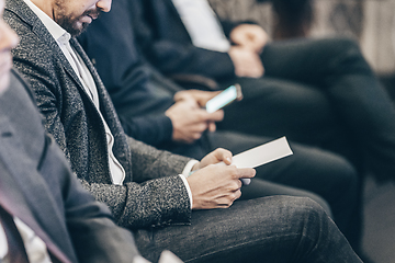 Image showing Businessman hands holding meeting brochure with program and schedules of business conference lectures. Event participants in conference hall.