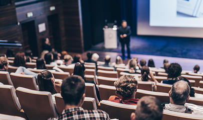 Image showing Speaker giving a talk in conference hall at business event. Rear view of unrecognizable people in audience at the conference hall. Business and entrepreneurship concept.