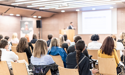 Image showing Speaker giving a talk in conference hall at business event. Rear view of unrecognizable people in audience at the conference hall. Business and entrepreneurship concept.