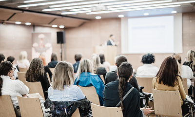 Image showing Speaker giving a talk in conference hall at business event. Rear view of unrecognizable people in audience at the conference hall. Business and entrepreneurship concept.