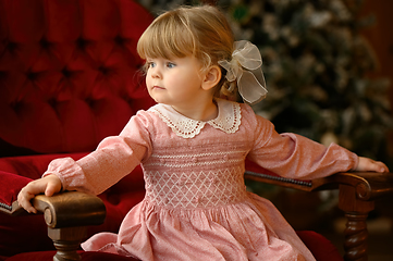 Image showing Little blond girl sits in a chair in front of Christmas tree