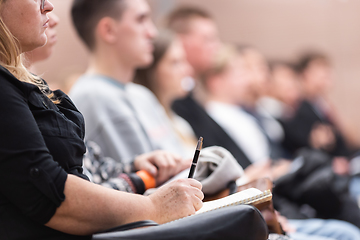 Image showing Female hands holding pen and notebook, making notes at conference lecture. Event participants in conference hall.