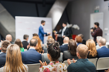 Image showing Business team leader receiving award prize at best business project competition event. Business and entrepreneurship award ceremony theme. Focus on unrecognizable people in audience.