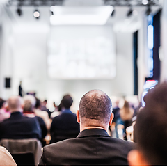 Image showing Speaker giving a talk in conference hall at business event. Rear view of unrecognizable people in audience at the conference hall. Business and entrepreneurship concept.