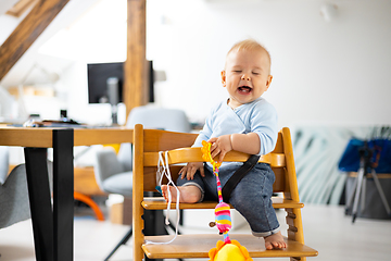 Image showing Happy infant sitting and playing with his toy in traditional scandinavian designer wooden high chair in modern bright atic home. Cute baby.