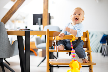 Image showing Happy infant sitting and playing with his toy in traditional scandinavian designer wooden high chair in modern bright atic home. Cute baby.