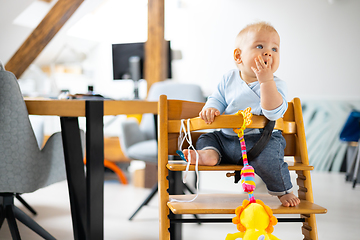 Image showing Happy infant sitting and playing with his toy in traditional scandinavian designer wooden high chair in modern bright atic home. Cute baby.