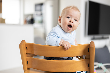 Image showing Happy infant sitting in traditional scandinavian designer wooden high chair in modern bright home. Cute baby.