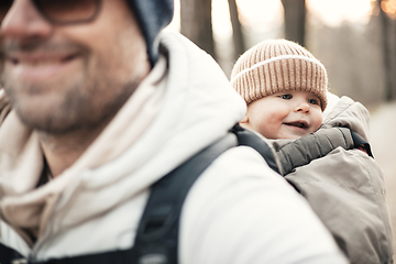 Image showing Sporty father carrying his infant son wearing winter jumpsuit and cap in backpack carrier hiking in autumn forest.